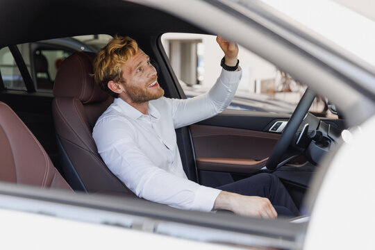 Smiling man customer buyer client in white shirt sit in car salon driving drive touch mirror chooses auto want buy new automobile in showroom vehicle dealership store motor show indoor Sales concept