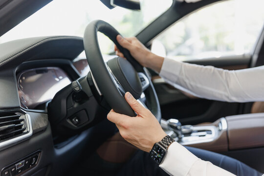 Close up cropped up photo shot hand customer buyer businessman client man wearing white shirt watch sitting in car salon hold steering wheel driving automobile modern vehicle Car sales driver concept.