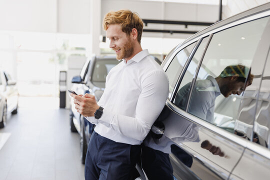 Man happy customer male buyer client wear white shirt talk mobile cell phone leaning on car choose auto want buy new automobile in showroom vehicle dealership store motor show indoor Sales concept