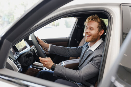 Satisfied man customer male buyer client wear classic grey suit driving car hold wheel choose auto want buy new automobile in showroom vehicle salon dealership store motor show indoor Sale concept