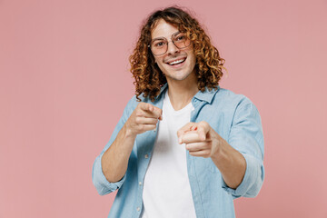 Young smiling happy satisfied man 20s with long curly hair wear blue shirt white t-shirt glasses point index finger camera on you say do it isolated on pastel plain pink color wall background studio