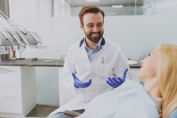 Young caucasian man dentist doctor in white gown talk speaking consulting patient woman sitting at...