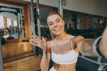 Close up young sporty athletic sportswoman woman in white sportswear warm up training sit near treadmill trainers do selfie shot on mobile cell phone wave hand in gym indoors Workout sport concept