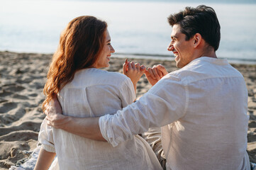 Happy smiling young couple two family man woman in white clothes hug sit on plaid little fingers friendship gesture rest relax together at sunrise over sea beach ocean outdoor seaside in summer day.