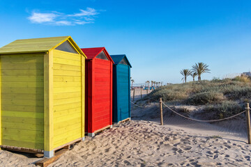 Obraz na płótnie Canvas Casetas de playa de maderera de colores amarillo, rojo y azul con palmeras de fondo y dunas canet de berenguer