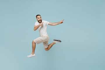 Fototapeta na wymiar Full length side view young happy man 20s wear casual white t-shirt jump high point index finger aside on workspace area mock up isolated on plain pastel light blue color background studio portrait