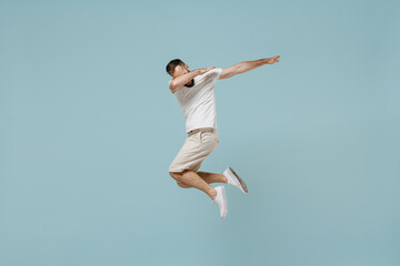 Obraz premium Full length young man 20s in casual white t-shirt jump high doing dab hip hop dance hands move gesture youth sign hide cover face isolated on plain pastel light blue color background studio portrait