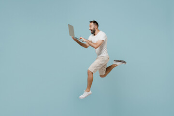 Full length side view young overjoyed man in casual white t-shirt jump high run fast hurrying up...