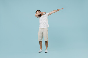 Obraz premium Full length young happy man 20s wearing casual white t-shirt doing dab hip hop dance hands move gesture youth sign hide cover face isolated on plain pastel light blue color background studio portrait.