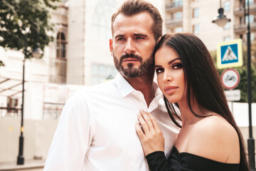 Beautiful fashion woman and her handsome elegant boyfriend in suit. Sexy brunette model in black evening dress. Fashionable couple posing in the street in Europe. Brutal man and his female outdoors