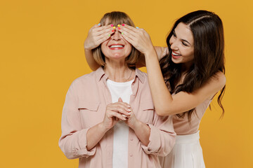 Two young smiling cheerful happy daughter mother together couple women in casual beige clothes close eyes with hands play guess who or hide and seek isolated on plain yellow color background studio.