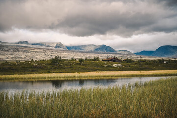 Scenic landscape in the Rondane National Park in Norway. Heathland and a lake with mountains in the background under a cloudy sky.