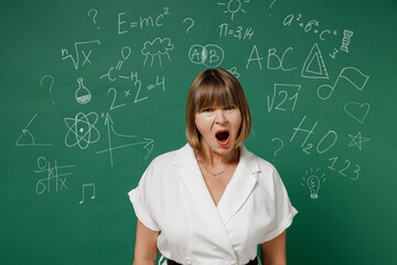 Displeased irritated teacher mature elderly senior elegant lady woman 55 wears white shirt scream isolated on green wall chalk blackboard background studio. Education in school September 1 concept.