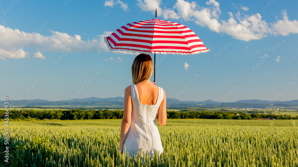 Wall mural young girl in hat with umbrella on green wheat field and mountains on background