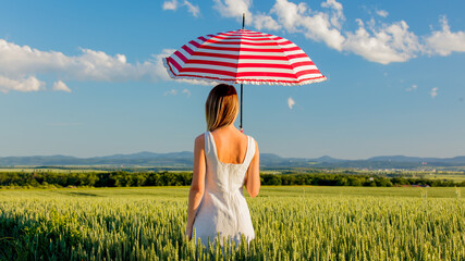 young girl in hat with umbrella on green wheat field and mountains on background