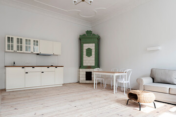 Interior of kitchen and dining room in spacious apartment with wooden floor, white wall and dining table. Industrial loft indoors with tiled stove.
