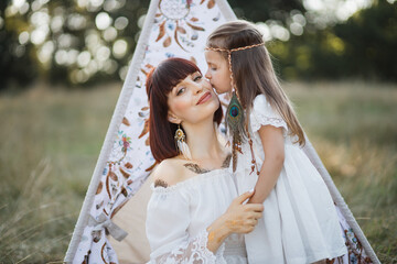 Outdoor shot of lovely Native American family near wigwam teepee in the field. Cute little girl...