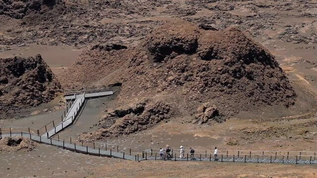 A group of people walking down a steep hillside on the volcanic island Bartolomeu, Galapagos Islands, Ecuador. People walk downhill on wooden walkways