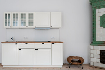 Modern kitchen with white cabinets and wooden counter in new apartment with wooden floor and tiled stove. Interior of cozy room in industrial loft.