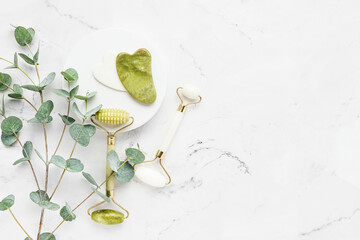 Gua Sha massager, jade facial rollers and eucalyptus branches on white marble background. SPA concept © Laima Gri