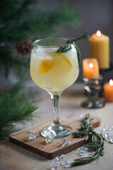 A big glass with christmas drink lemonade with rosemary and lemons surrounded by christmas decoration, lights and candles