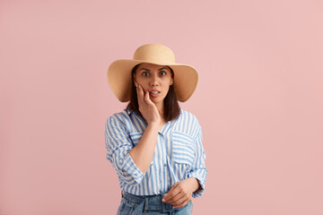 Oh no. Worried woman with dark forgot something, needs solution for improvement, to correct her mistake, wears straw hat, striped shirt, jeans with belt, on pink background. Summer emotions concept.