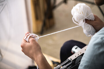 Cropped view of artisan holding thread near carpet tufting gun and canvas 