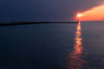 Obraz premium Setting sun seen from the beach in Darłówko, Poland. Beautiful seascape. Two yachts and wooden breakwater on the horizon.