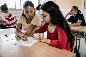 Two latin and hispanic female classmates friends together in the High School Classroom during an exam