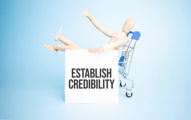 Wooden Doll in a shopping with white paper and ESTABLISH CREDIBILITY sign. Business concept