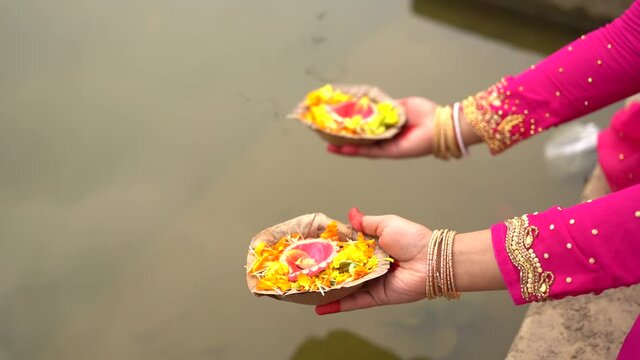 Closeup of hands of unrecognized women holding diya for aarti near river water, prayer for indian gods