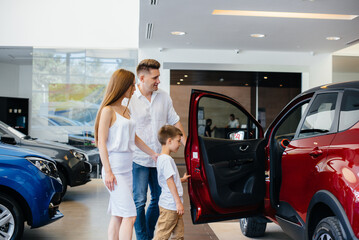 A happy young family chooses and buys a new car at a car dealership. Buying a new car