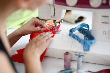 Woman sew on red fabric on a sewing machine