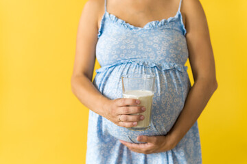 Motherhood, femininity, vitamins, calcium, healthy eating food, dairy, hot summer - croped portrait pregnant unrecognizable woman in floral blue dress holds drink glass of milk on yellow background
