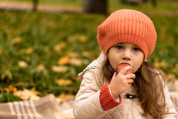 Close Up Portrait Of Little Cute Preschool Minor Girl In Orange Beret On Yellow Fallen Leaves Eats Red Apple Look At Camera Cold Weather In Fall Park. Childhood, Family, Motherhood, Autumn Concept