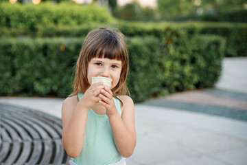 Fototapeta premium girl in a light dress eats popsicle ice cream in a city park. Children's rest in the summer.