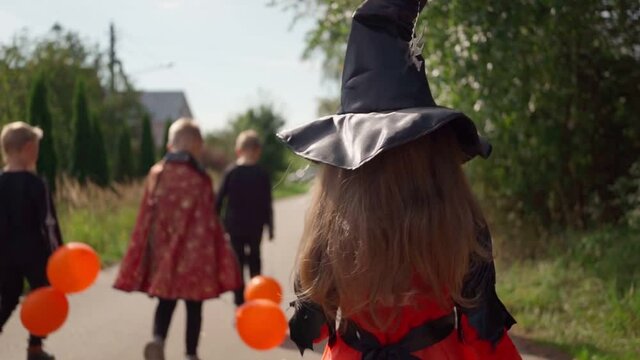 Halloween kids going to collect candy. Trick-or-treating. Guising. Jack-o-lantern. Children in carnival costumes outdoors. Witch and skeletons. Friends with orange balloons. celebrate halloween
