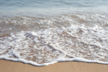 Blurred neutral sea coast background. The wave hits the sand with bubbling foam