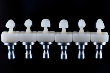 Six upper jaw frontal ceramic crowns prosthesis on black glass background. Artificial jaw with veneers and crowns. © gorynvd