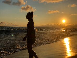 Young girl watching the sunset at Barra da Tijuca beach in Rio de Janeiro, Brazil. Sea with calm waves.