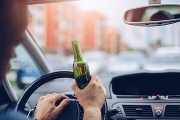 Drunk adult man drives a car with a bottle of beer. Driver under alcohol influence.