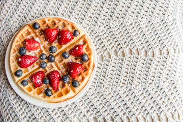 Waffle with blueberries and strawberries on a crochet background