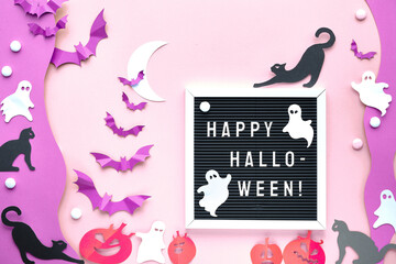 Text Happy Halloween on letter board, letterboard. Cute background with black cats, vibrant purple paper bats, pink pumpkins, white ghosts. Flat lay on pink and purple paper with white Crescent Moon.