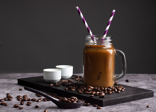 Vaso de caf&eacute; con leche con dos popotes y crema sobre un fondo oscuro