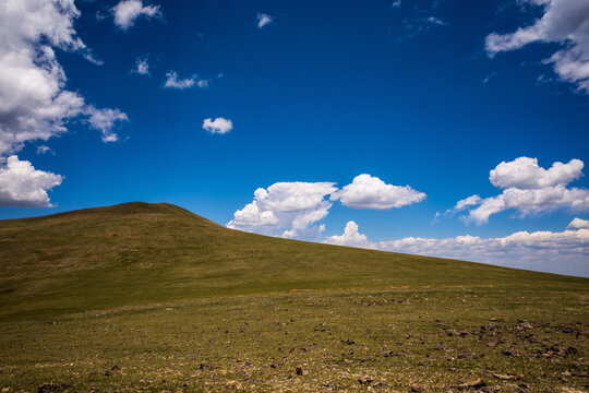 Green mountain hillside in remote area in the Rocky Mountains against blue sky and white clouds.