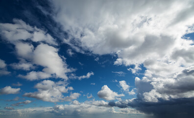 Obraz premium White fluffy clouds moving softly across the sky. Clear blue sky is being gradually covered with clouds in bright sunshine, some stormy clouds appearing in the end.
