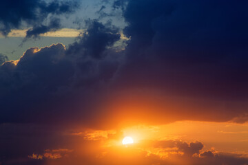 Fototapeta premium Beautiful view of the sun going down among the moving clouds. Close up view to the sunset and picturesque clouds of bright orange and yellow colors that gradually fade in the end.