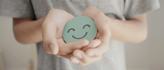 Hand holding green happy smile face paper cut, mental health assessment, child positive wellness, teen wellbeing, world mental health day, mindfulness concept - 453694757