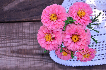 pink zinnia flowers on a wooden background next to a vintage-style napkin selective focus