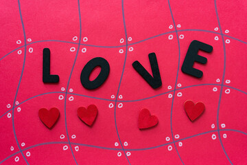 the word love in black chalk letters and hand painted red hearts on a red grid paper background